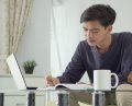 young asian man working from home taking notes