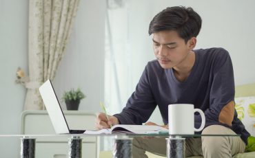 young asian man working from home taking notes