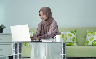 asian woman in hijab working from home using her laptop