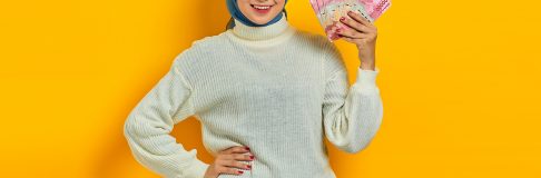 Smiling beautiful Asian Muslim woman in white sweater holding ca