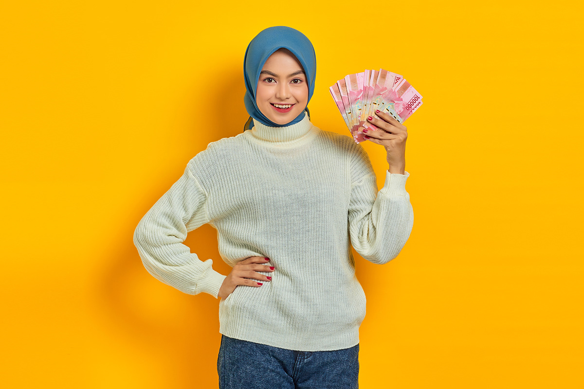 Smiling beautiful Asian Muslim woman in white sweater holding ca