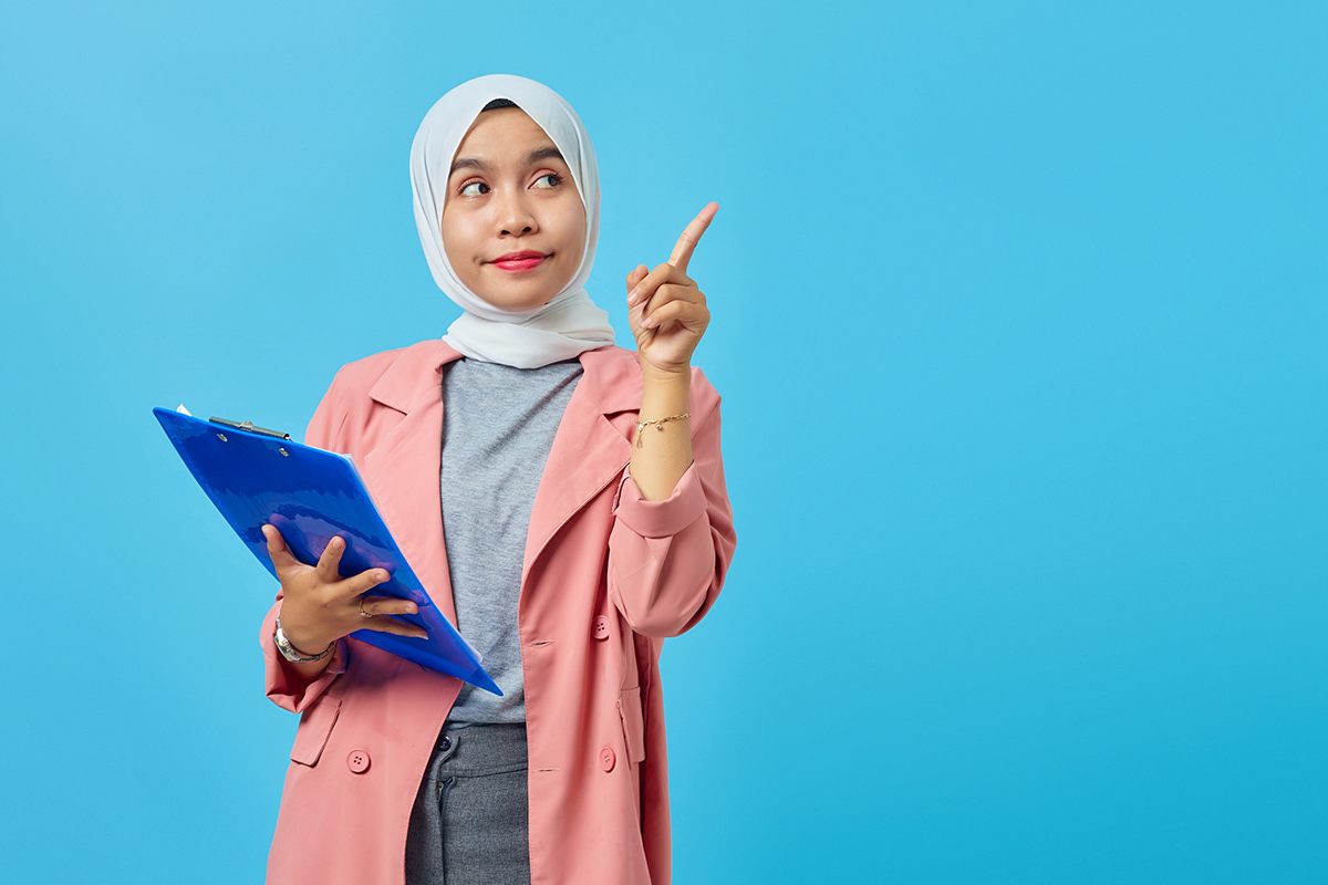 Portrait of a beautiful smiling woman holding a folder standing and pointing to an empty space on a blue background