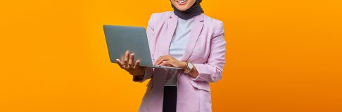 Portrait of smiling asian woman holding laptop and looking at camera over yellow background